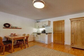 A compact kitchen with white cabinets, a wooden dining table with chairs, and a large wooden wardrobe. - "Fellhorn" in the Schneider house (Riezlern)