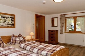 A bedroom with two beds, a wooden wardrobe, a mirror, and a window with curtains. - "Fellhorn" in the Schneider house (Riezlern)