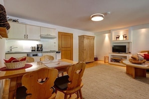 A modern kitchen with white cabinets, a dining area with wooden chairs, a television, and a fireplace. - "Fellhorn" in the Schneider house (Riezlern)