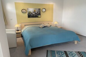 A bedroom with a bed, two bedside lamps, a nightstand, a wall-mounted picture, and a patterned rug. - Holiday apartment with 2 bedrooms (Butjadingen)