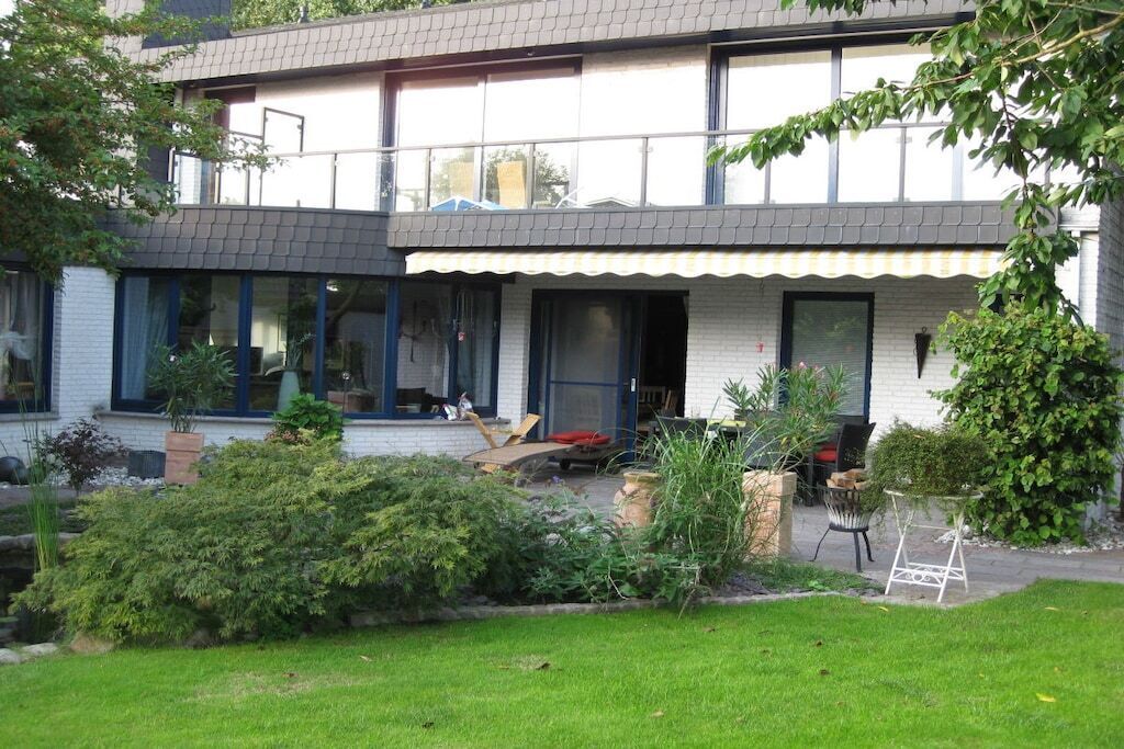 A two-story house with a covered porch, a lawn, and various potted plants.