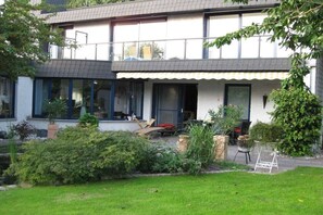 A two-story house with a covered porch, a lawn, and various potted plants. - Holiday apartment with 2 bedrooms (Butjadingen)