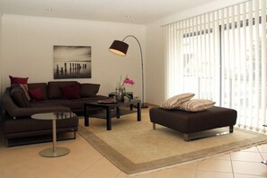 A modern living room with a sofa, ottoman, coffee table, and floor lamp. - Holiday apartment with 2 bedrooms (Butjadingen)
