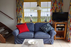 Un salon comprenant un canapé, un téléviseur, un meuble en bois et une fenêtre avec des rideaux.