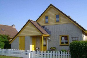 A two-story house with a white picket fence, a yellow front door, and a brick exterior. - Holiday home with 2 bedrooms (Julianadorp aan Zee)