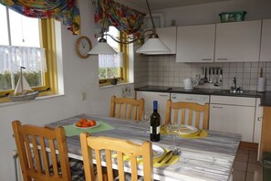 A dining table with chairs, a wine bottle, and a clock on the wall. - Holiday home with 2 bedrooms (Julianadorp aan Zee)