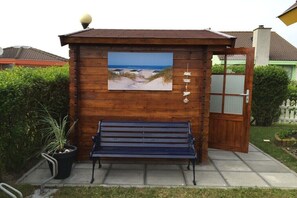 Une structure en bois avec un banc, une image d’une plage et une porte dont les panneaux sont en verre dépoli.