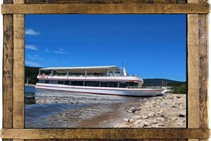 Ein Flussdampfer mit überdachter oberer Deck, liegt an einem felsigen Ufer, im Hintergrund ein klarer, blauer Himmel.