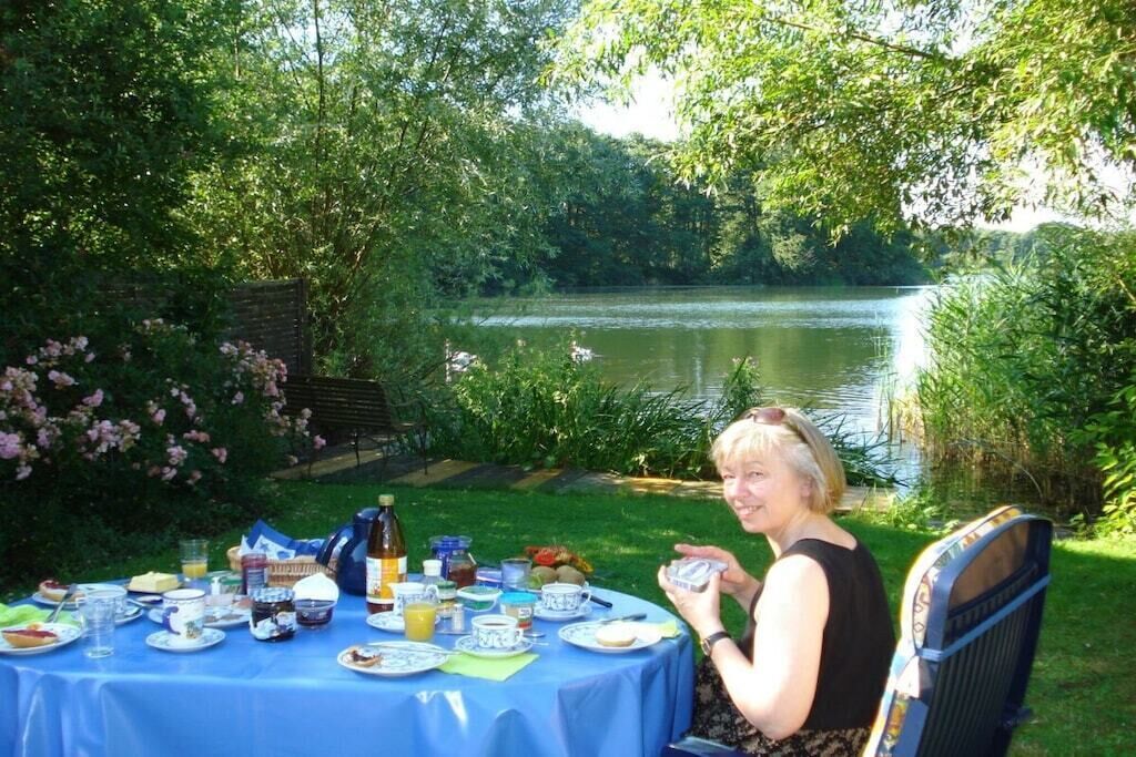 A person seated at a table with a view of a lake and greenery.