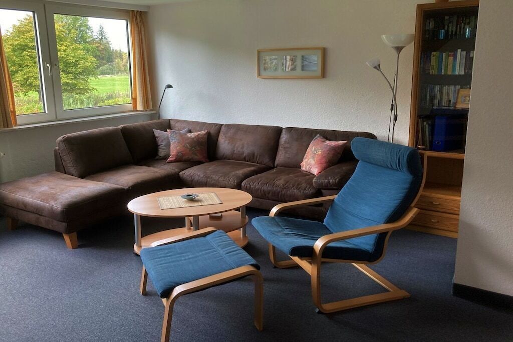 Ein Wohnzimmer mit einer Eckcouch, zwei Sesseln, einem kleinen runden Tisch und einem Bücherregal.