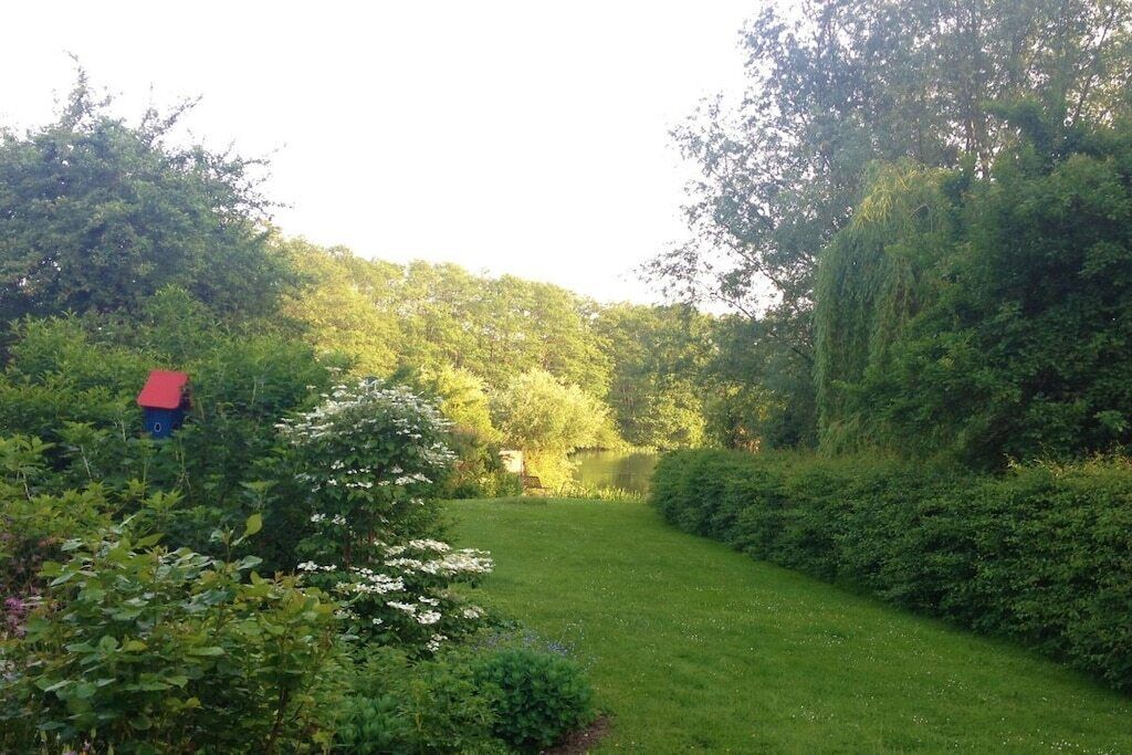 Un jardín con un estanque, rodeado de abundante follaje y una pequeña construcción roja.