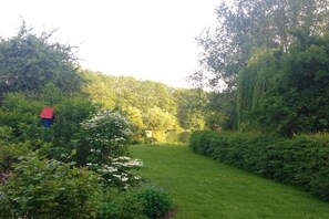 Een tuin met een vijver, omringd door weelderige begroeiing en een klein rode gebouw.