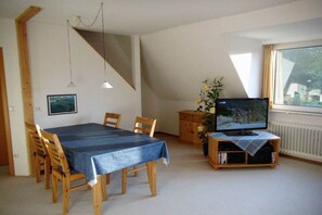 A dining area with a table and chairs, a television on a wooden stand, and a window with curtains. - Holiday apartment with 2 bedrooms (Timmdorf)