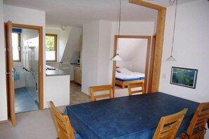 Een kamer met een eettafel, stoelen, een bed en een kitchenette.