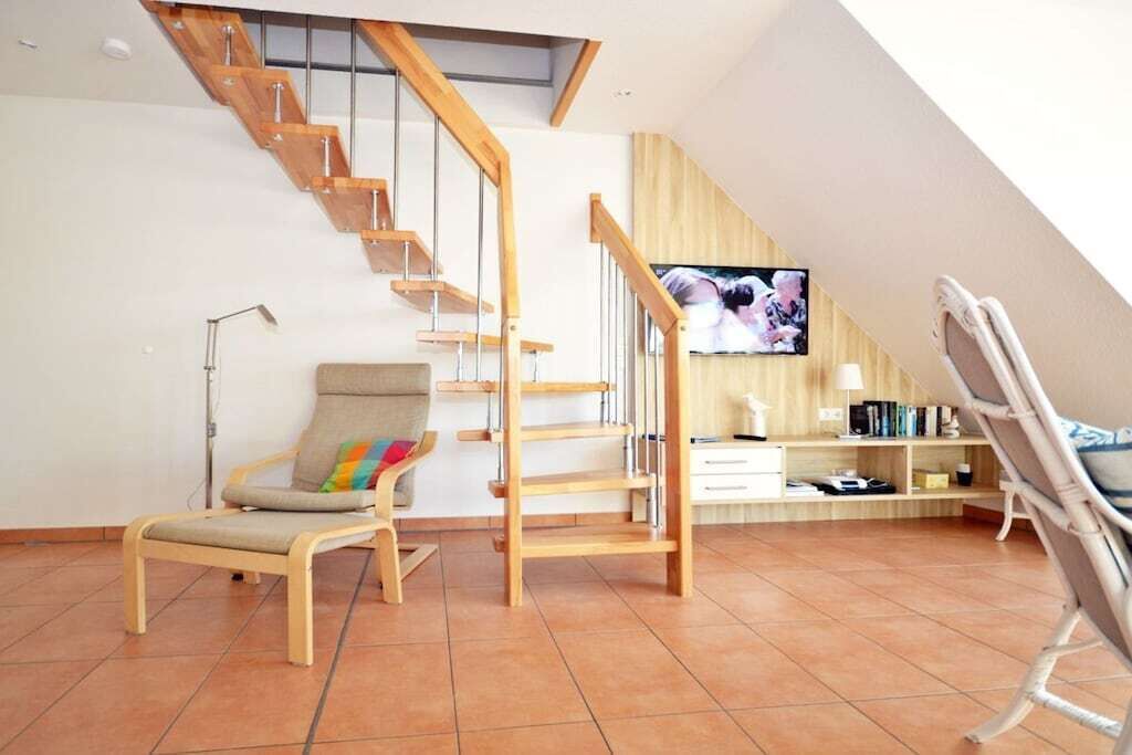 Ein Wohnzimmer mit einer Holztreppe, einem Fernseher, einem Sessel und einem Bücherregal.