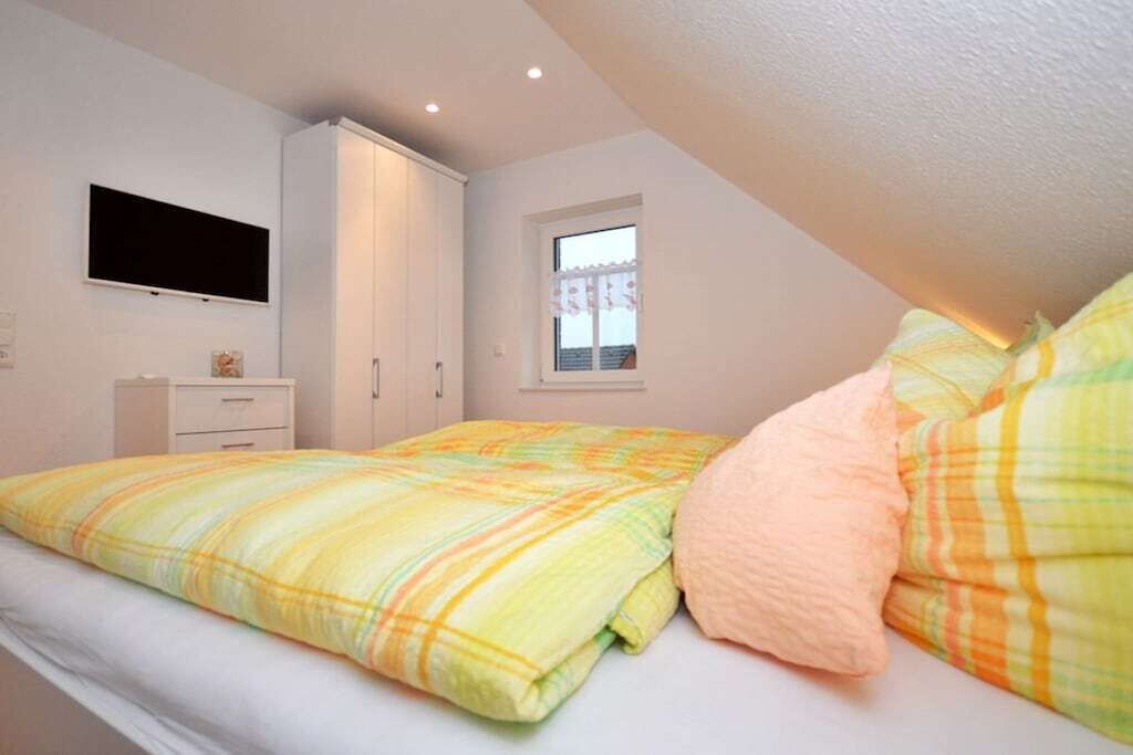 Un dormitorio con cama, televisión montada en la pared, ventana con cortina y armario.