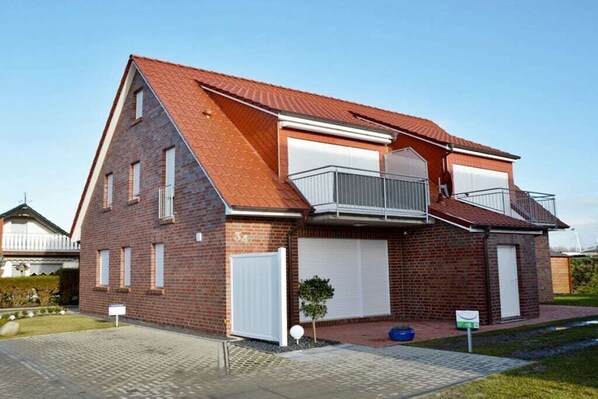 A two-story brick house with a red roof, a balcony on the upper floor, and a garage door. - Holiday apartment with 1 bedroom (Norddeich)