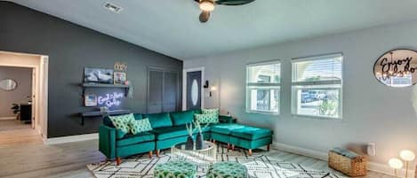 A modern living room with a sectional sofa, ottomans, a patterned rug, and a ceiling fan.