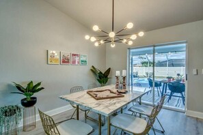Un espace repas comprenant une table en marbre, des chaises, un lustre et une vue sur l’extérieur, accessible par des portes vitrées.