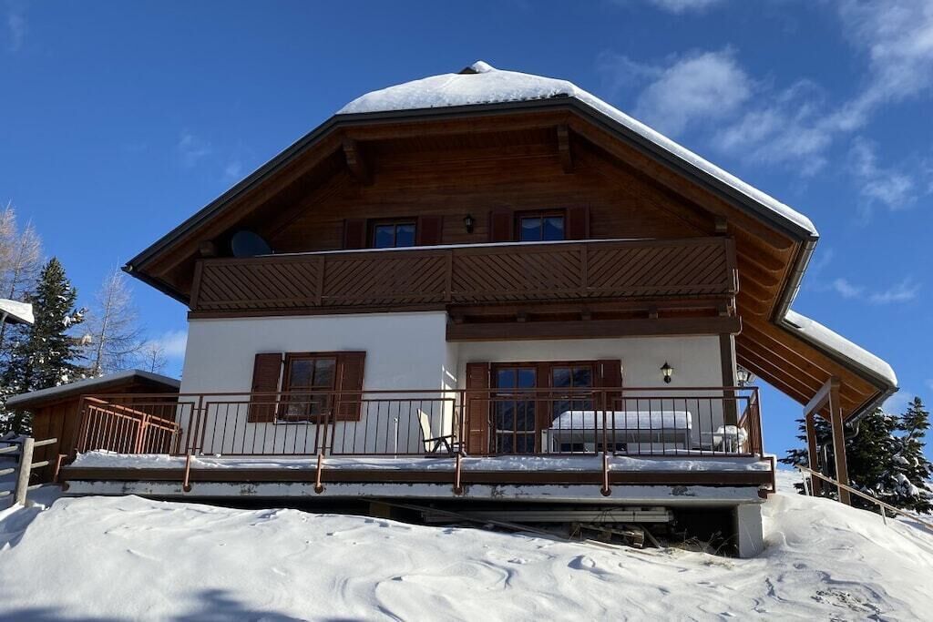 A two-story wooden chalet with a balcony, set against a clear sky.