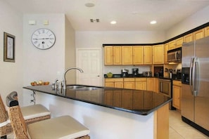 A kitchen with wooden cabinets, a stainless steel refrigerator, a built-in oven, and a clock on the wall. - Villa in Cape Coral with swimming pool (Cape Coral)