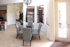 A dining area with a glass table and four chairs, a chandelier, and a view through large windows. - Villa in Cape Coral with swimming pool (Cape Coral)