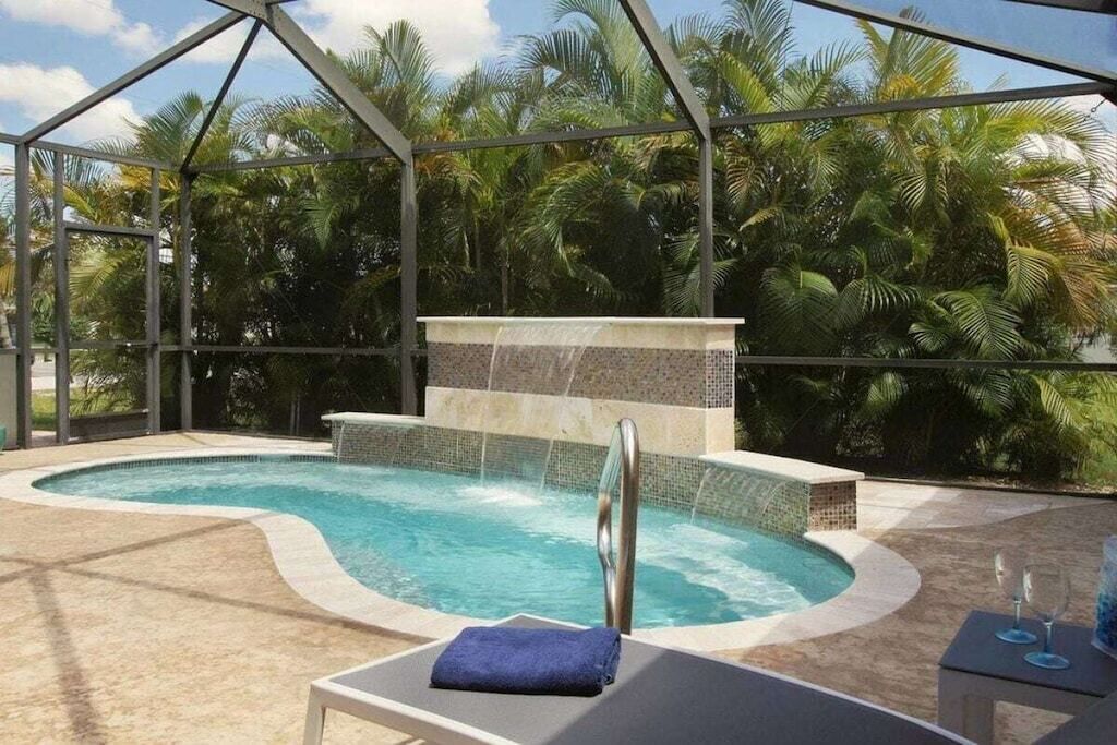 A swimming pool with a waterfall feature, surrounded by palm trees.