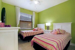 Une chambre avec deux lits, une table de chevet, une lampe et un ventilateur de plafond.