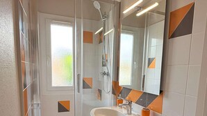 Un bany modern amb plat de dutxa de vidre, un lavabo blanc i un mirall gran.