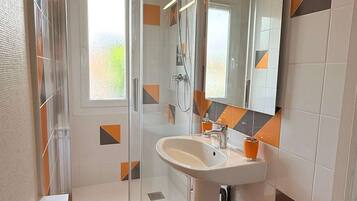 Un bany modern amb plat de dutxa de vidre, un lavabo blanc i un mirall gran.