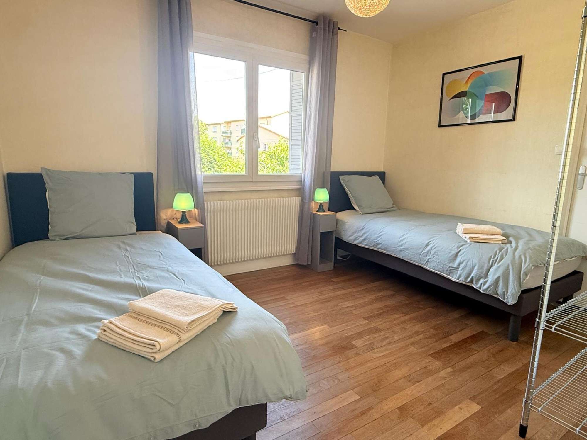 Ein Zimmer mit zwei Betten, einem Heizkörper, einem Fenster mit Vorhängen, einem Wandbild und einem Heizkörper auf dem Boden.
