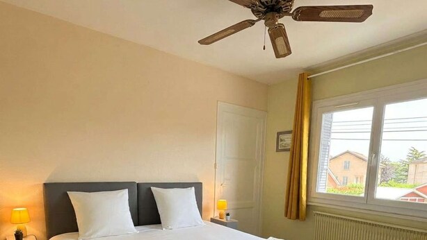 Habitació d'hotel amb un llit gran, dues làmpades de nit, un ventilador de sostre, una finestra amb cortines i un radiador.