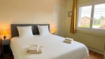 Habitació d'hotel amb un llit gran, dues làmpades de nit, un ventilador de sostre, una finestra amb cortines i un radiador.