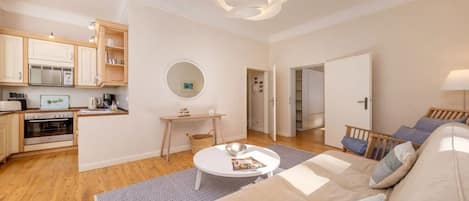 Una sala de estar moderna con sofá, una mesa de centro y una zona de cocina con armarios de madera y electrodomésticos.