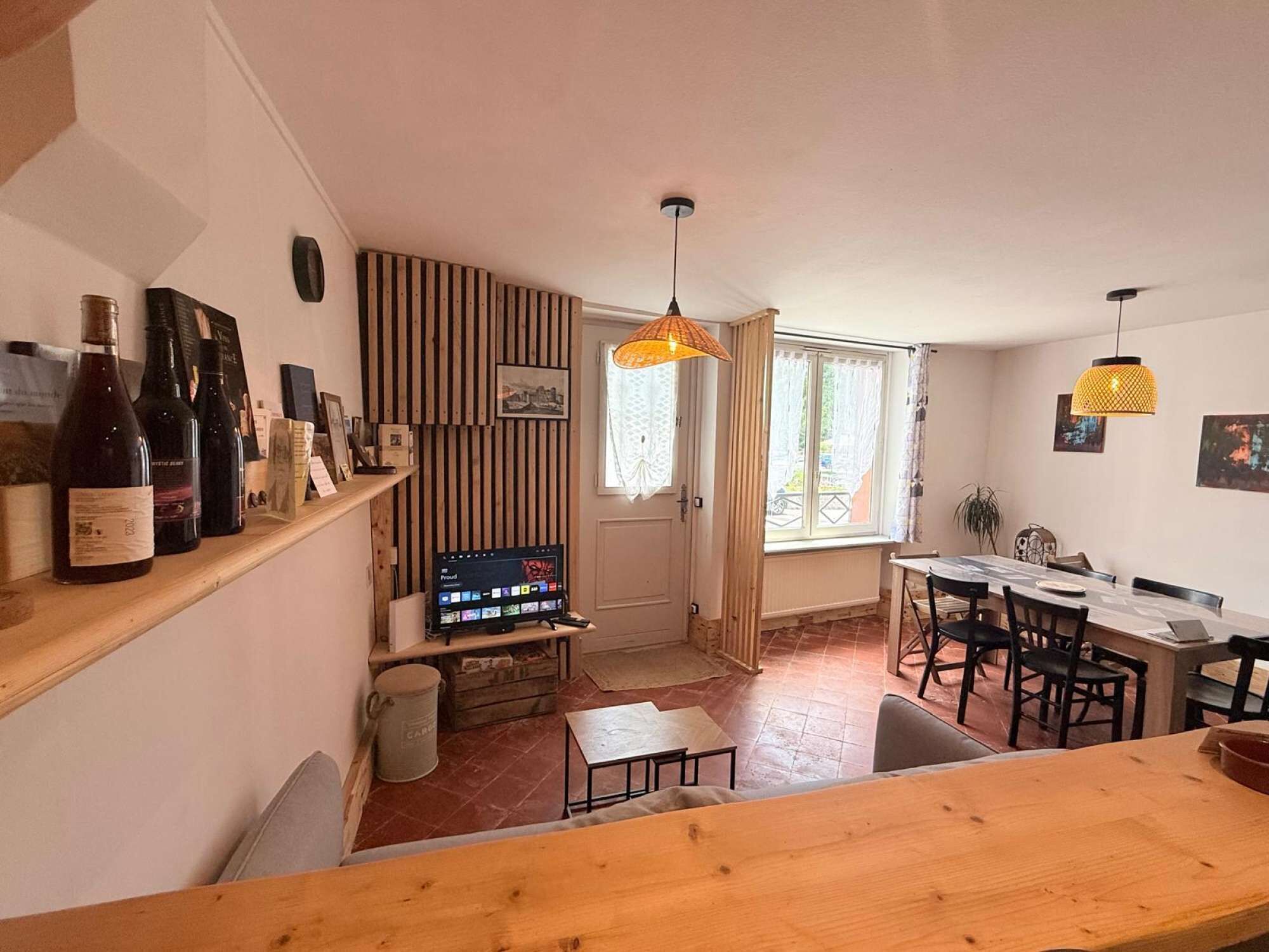 Een gezellige woonruimte met een houten tafel, een televisie en een wijnrek met flessen.