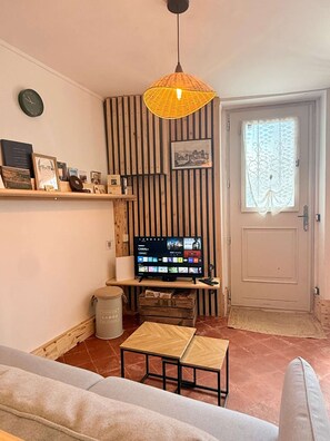 Una sala de estar con televisor, sofá, una mesita, una lámpara decorativa colgante y una puerta con ventana.
