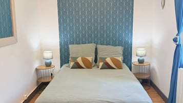 Een slaapkamer met een bed, twee nachtkastjes, een kroonluchter en een behang met patroon.