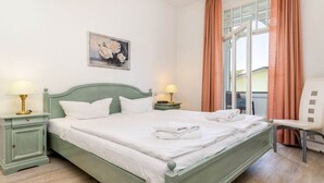 Ein ordentlich bezogenes Bett mit weißen Leinen, zwei Nachttische mit Lampen, ein Stuhl und ein Fenster mit Vorhängen.