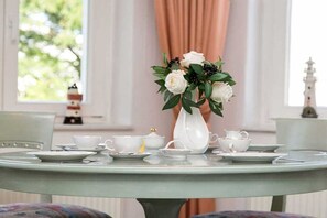 Ein runder Tisch mit einer weißen Vase, die weiße Blumen und grüne Blätter enthält, umgeben von weißen Teetassen und Untertassen.