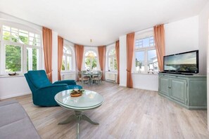 A spacious living area with a glass table, a teal armchair, and a television. - "Charlotte" at Villa Metropol (Binz)
