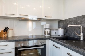 A modern kitchen with white cabinets, a stainless steel oven, a coffee maker, and a sink with a faucet.