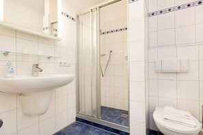 Kylpyhuone, jossa on lasiseinällä varustettu suihku, peilillä varustettu pesuallas ja wc.