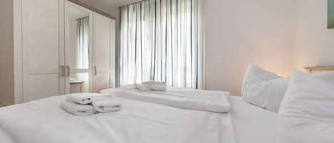 A hotel room with two beds, a wardrobe, and a large window with curtains.