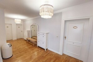 Une pièce avec un plancher en bois, des murs blancs, un banc, une commode, un miroir et une porte avec une plaque nominative.