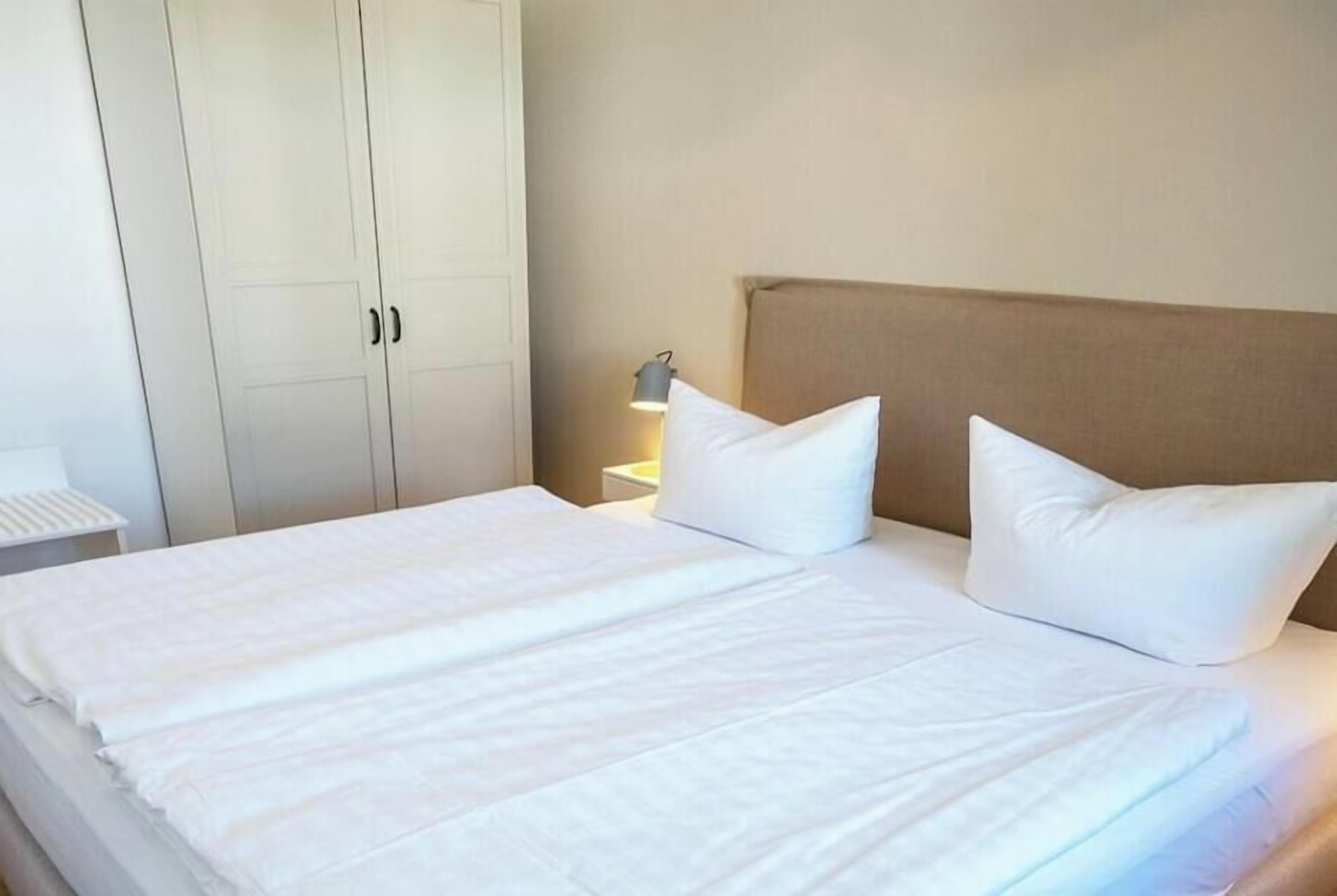Ein Hotelzimmer mit Bett, weißer Bettwäsche, einem Nachttisch mit Lampe und einem Kleiderschrank.