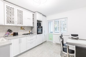 A modern kitchen with white cabinetry, a gas stove, a microwave, and a window with a view of trees.