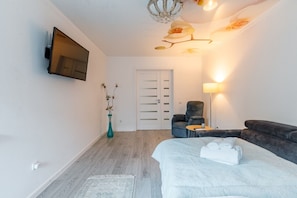 Habitación de hotel con cama, zona de estar con una silla y una mesa, un florero con flores, un televisor de pantalla plana montado en la pared y una puerta con diseño a rayas.