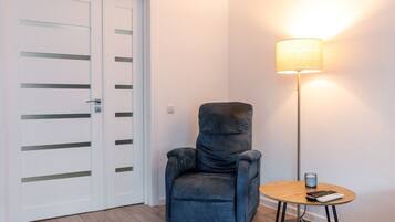 Een kamer met een blauwe fauteuil, een klein rond tafeltje met een lamp en een witte deur met horizontale lijnen.