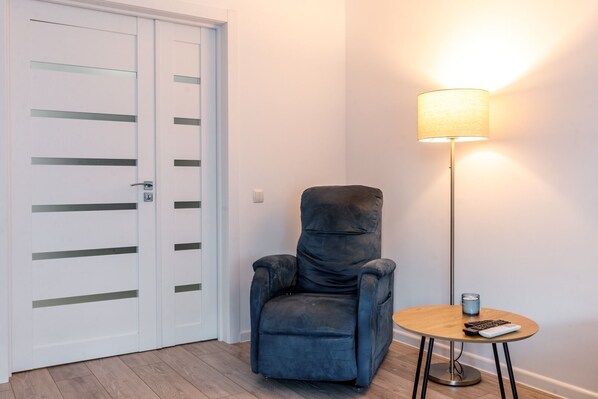 A room with a blue armchair, a small round table with a lamp, and a white door with horizontal lines. - Studio in New Building • Elevator • Quiet Retreat (Chișinău)