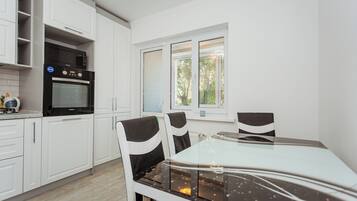 Een moderne keuken met witte kasten, een inbouwoven en een eethoek met een glazen tafel en stoelen.
